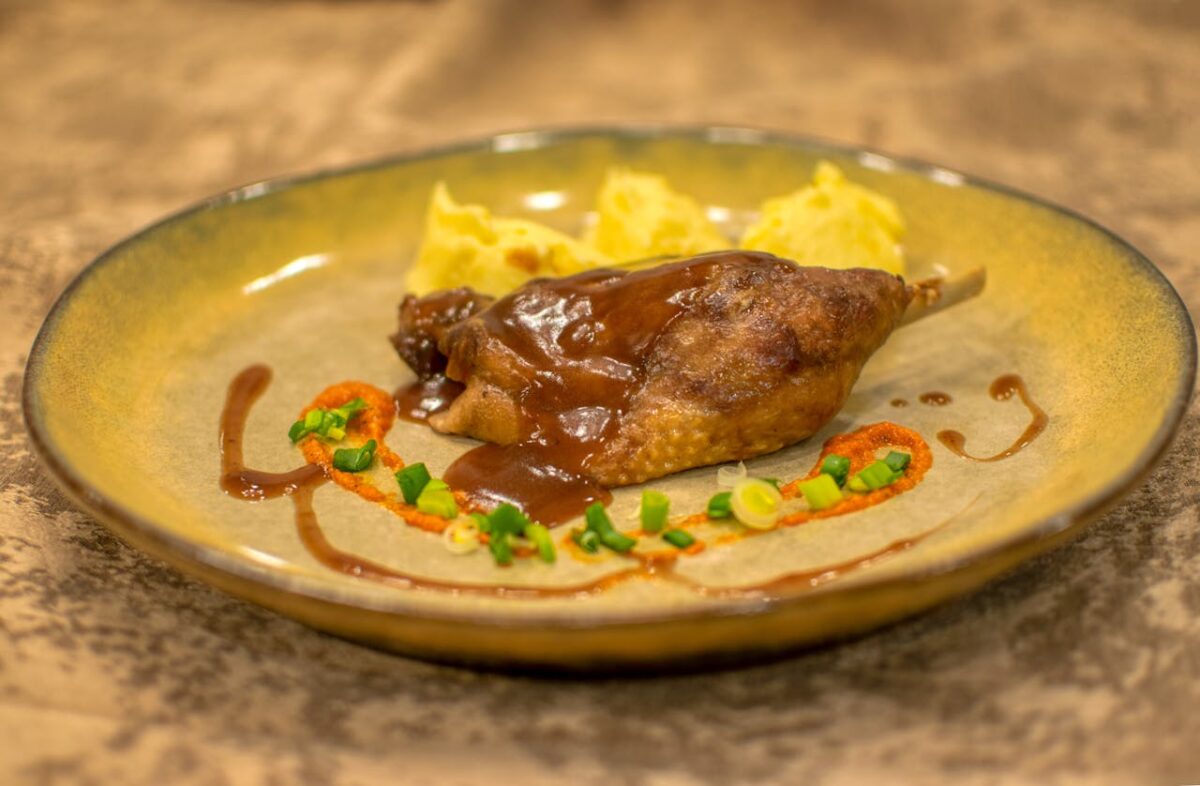 Delicious roasted duck leg with sauce and mashed potatoes garnished with vegetables.