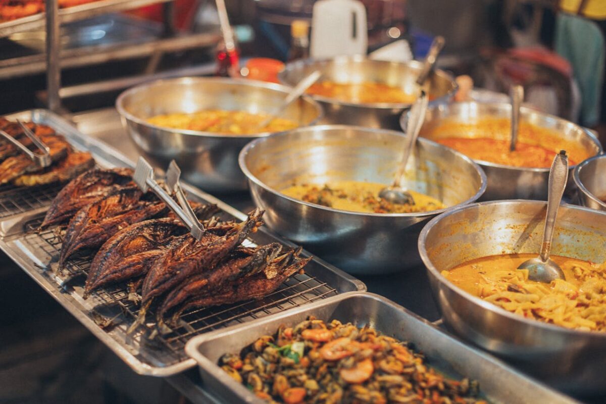 A colorful array of Asian street food dishes in metal bowls on display, showcasing diverse flavors.