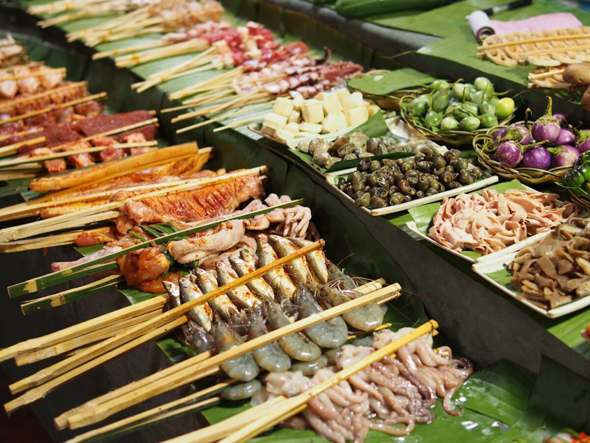 A vibrant display of skewered seafood and vegetables on banana leaves at an outdoor market.